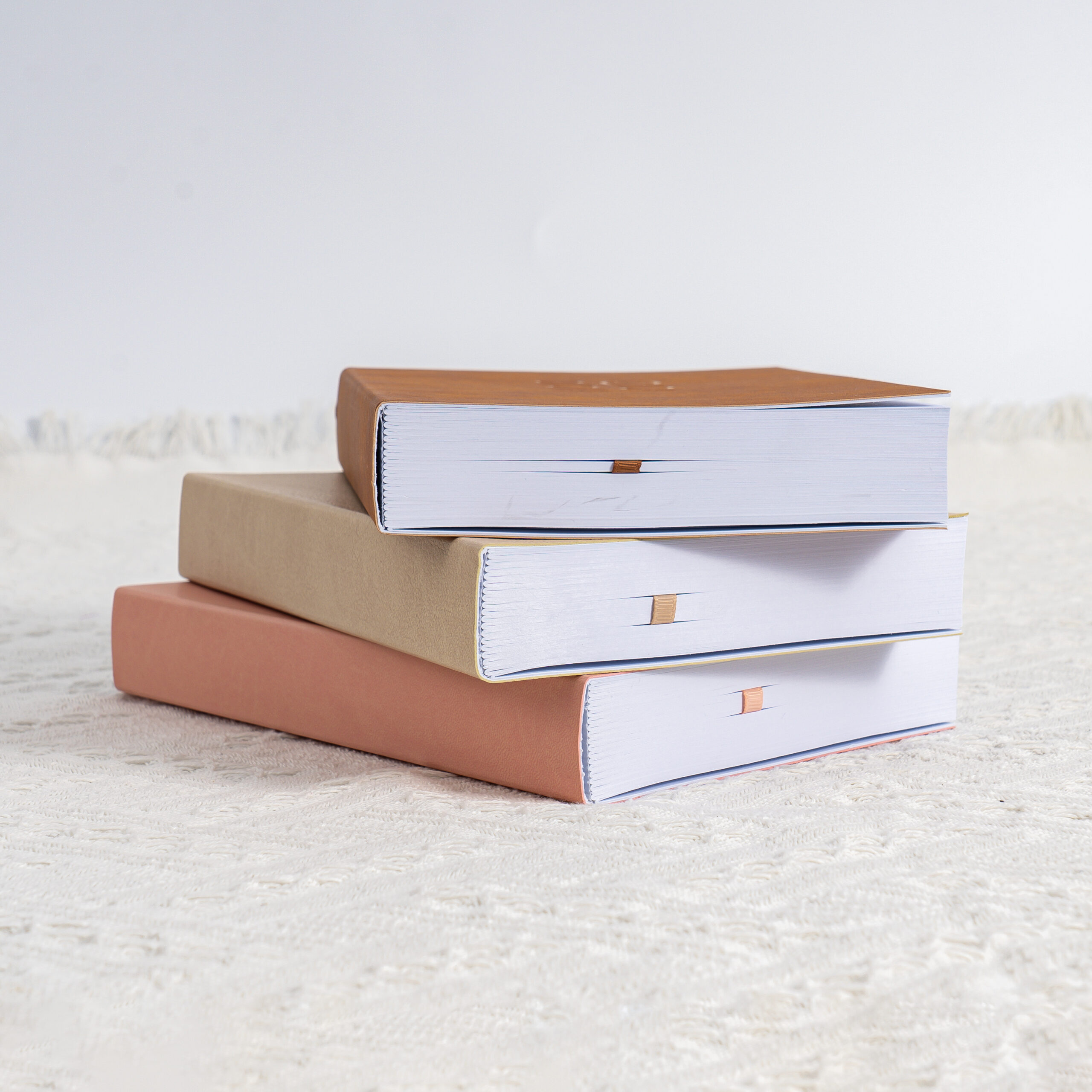 Three cloth covered hardcover books stacked with square board edges flush and ribbon markers showing at the spine