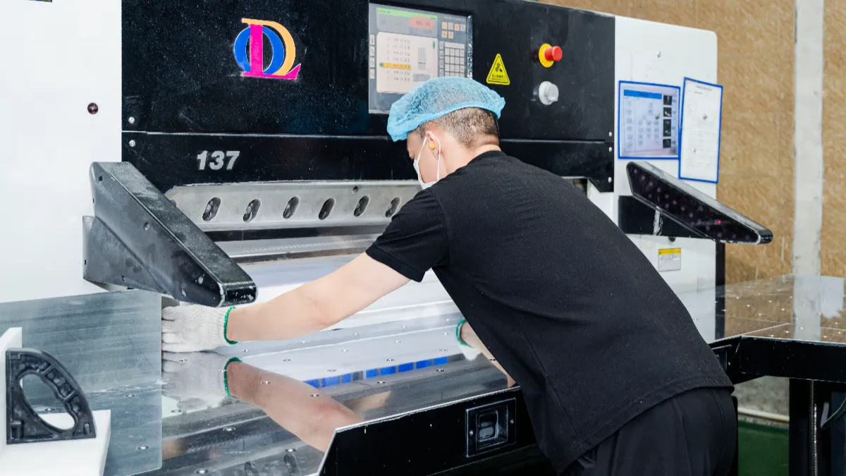 A worker in a hairnet, mask, and gloves feeding a stack of white sheets into a programmed automatic cutting machine labelled 137