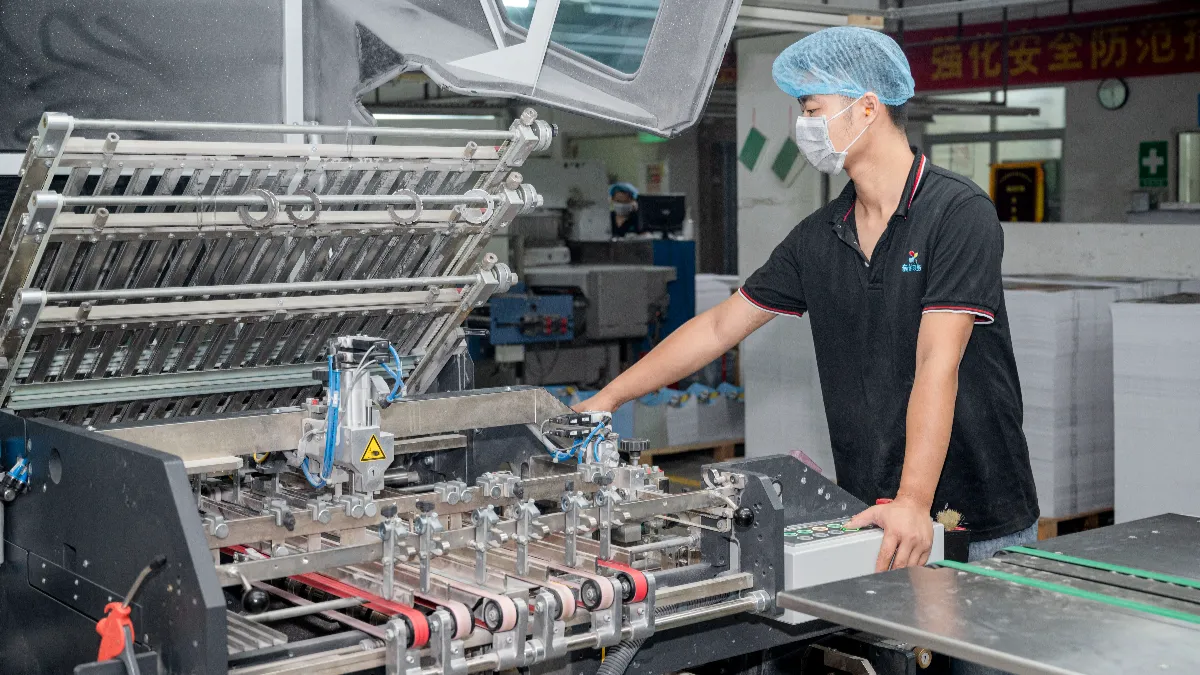 Operator feeding paperboard sheets into a mounting machine