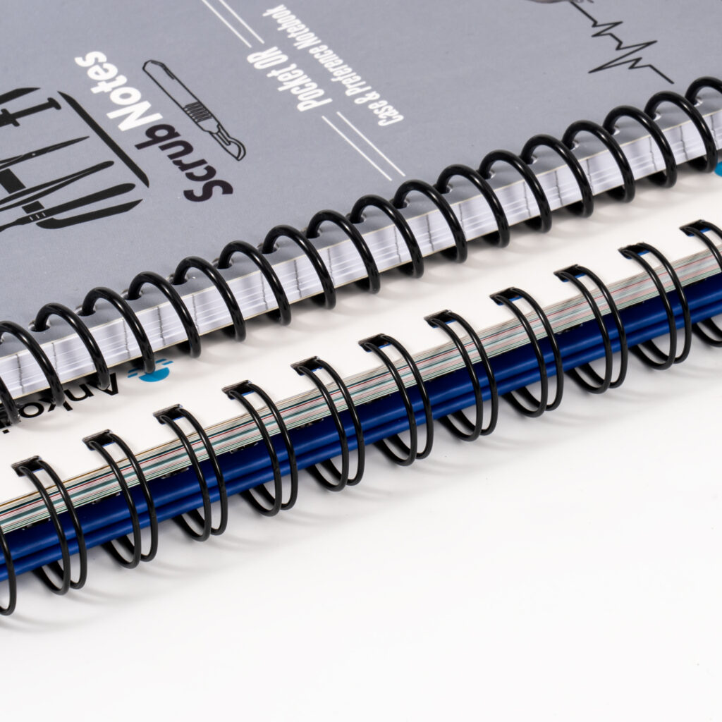 Grey printed notebook covers bound along the edge with black twin loop wire, stacked on a white surface