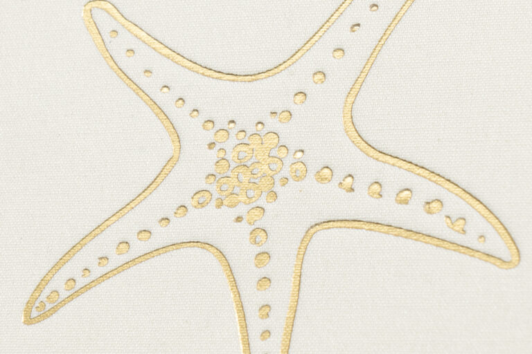 Gold foil starfish stamped on white cloth with the weave visible around it