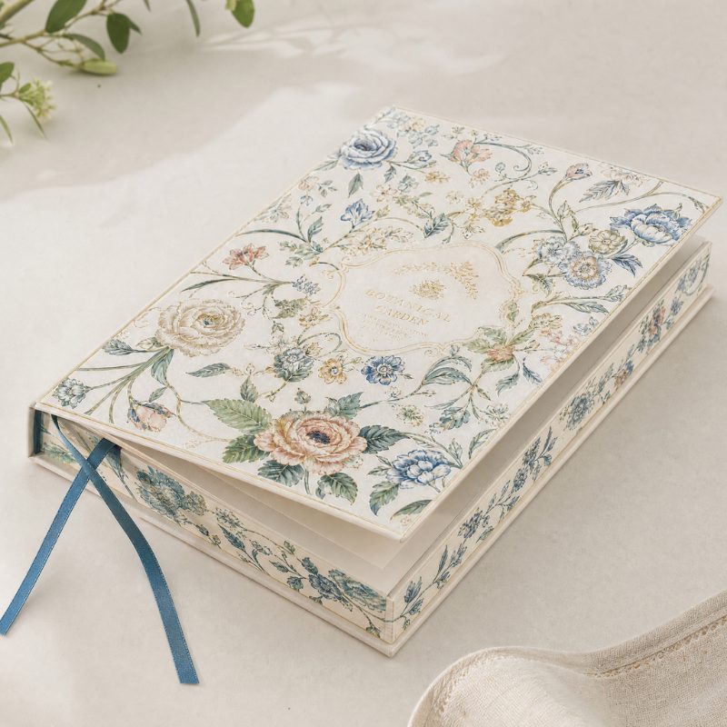 Two cream journals with a floral printed paper wrap and gold foil titles, tied with blue ribbon markers