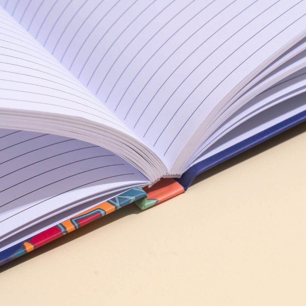 Close-up of an open ruled notebook showing how the pages fan at the spine joint against a patterned cover